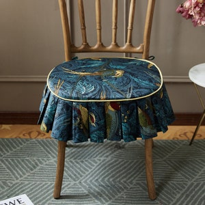 May include: A blue and green patterned chair cushion with a yellow trim and a ruffled edge. The cushion is made of fabric and has a floral design with birds.