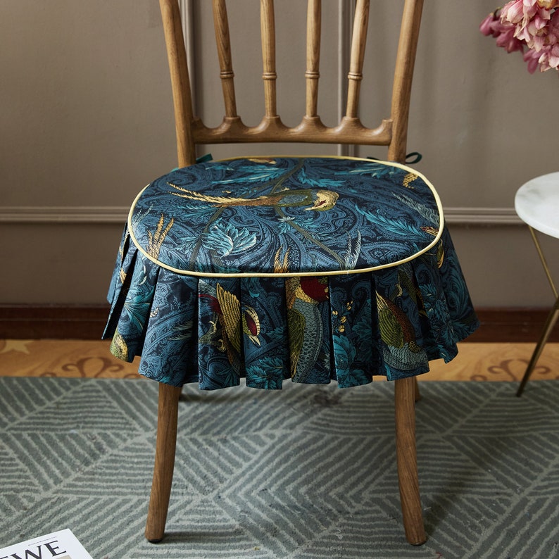 May include: A blue and green patterned chair cushion with a yellow trim and a ruffled edge. The cushion is made of fabric and has a floral design with birds.