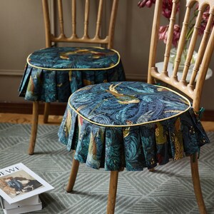May include: Two wooden chairs with blue and green patterned seat cushions. The cushions have a yellow trim and a ruffled edge. The chairs are on a patterned rug.