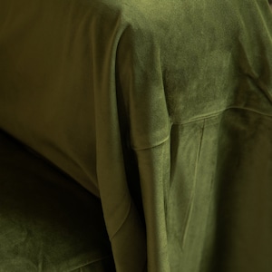 May include: Close-up of olive green velvet fabric. The fabric is draped, showing folds and texture. The color is a rich, deep green, and the material appears soft and luxurious. The image highlights the fabric's sheen and depth.
