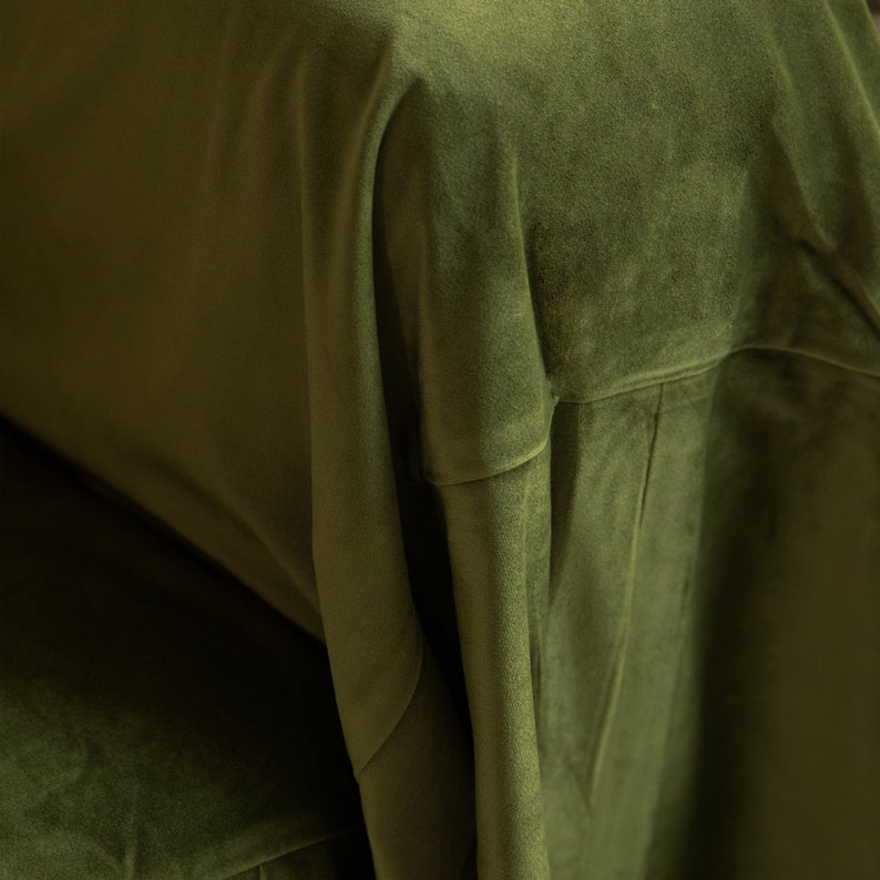May include: Close-up of olive green velvet fabric. The fabric is draped, showing folds and texture. The color is a rich, deep green, and the material appears soft and luxurious. The image highlights the fabric's sheen and depth.