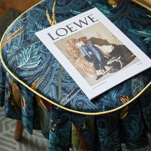 May include: A blue and gold patterned stool with a yellow trim and a magazine titled "LOEWE" on top.