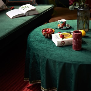 May include: A green velvet tablecloth with a book, a bowl of red apples, a candle, and a cup and saucer on a table.