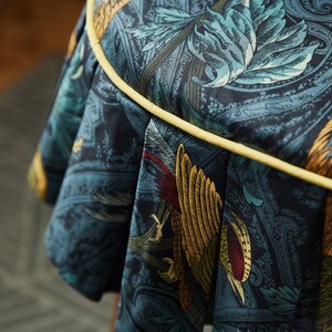 May include: A round, blue and gold fabric stool with a yellow trim. The fabric features a paisley pattern with birds and leaves.