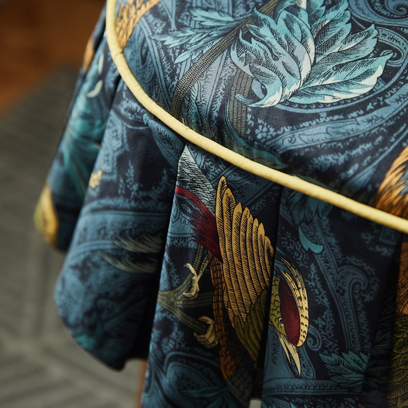 May include: A round, blue and gold fabric stool with a yellow trim. The fabric features a paisley pattern with birds and leaves.