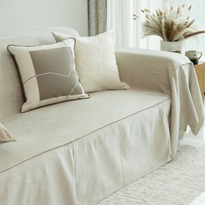 May include: A light beige linen sofa with a matching linen throw and two decorative pillows. One pillow is beige with a geometric pattern and the other is white with a textured design.