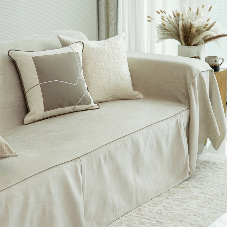 May include: A light beige linen sofa with a matching linen throw and two decorative pillows. One pillow is beige with a geometric pattern and the other is white with a textured design.