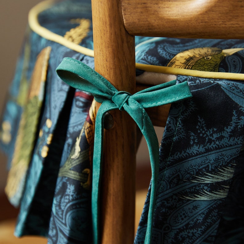 May include: A wooden chair with a dark blue and green patterned fabric seat and back. The chair has a green fabric tie that is tied around the back of the chair.