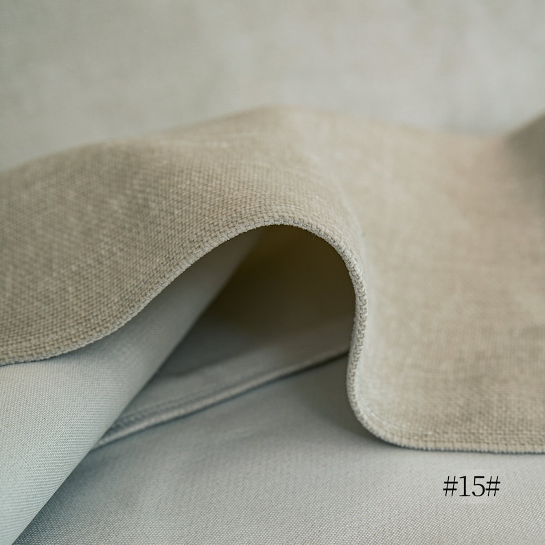 May include: Close-up of a light beige fabric with a soft, textured surface. The fabric is folded over itself, creating a curved shape. The fabric is #15#.