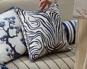 May include: A white and blue striped throw pillow with a fringe border. The pillow is on a couch with a striped fabric.