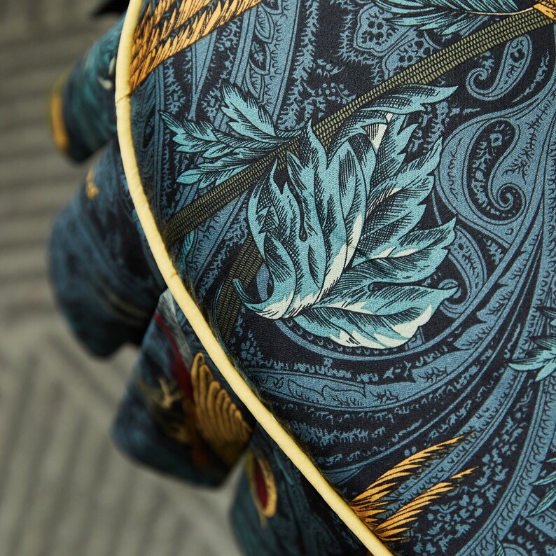 May include: Close-up of a blue and gold paisley patterned fabric with a yellow trim. The fabric features a large leaf design in the center.