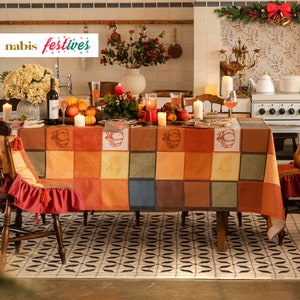 Könnte beinhalten: Ein Thanksgiving-Tischgedeck mit einer karierten Tischdecke mit Kürbisdesign. Der Tisch ist mit Kerzen, Weingläsern und verschiedenen Herbstdekorationen gedeckt. Der Tisch ist von Stühlen mit roten Kissen umgeben.