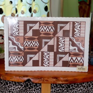 May include: A package of 12 place mats featuring a brown and white geometric design. The mats have a scalloped edge and are presented on a wooden table. The package is labelled "12 PLACE MATS". The mats measure 30.5cm x 45.7cm.