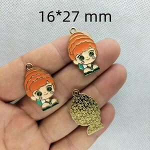 K&ouml;nnte beinhalten: Drei goldfarbene Metall-Anh&auml;nger, jeder mit einem Cartoon-M&auml;dchen mit orangefarbenen Haaren, gr&uuml;nen Augen und einem gr&uuml;nen Kleid. Die Anh&auml;nger sind 16 mm x 27 mm gro&szlig;.