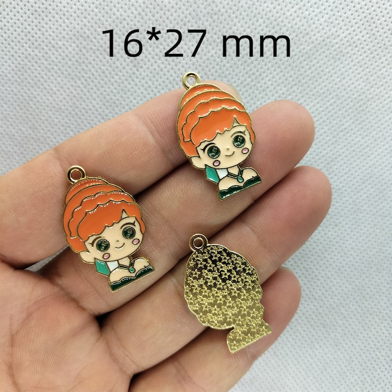 K&ouml;nnte beinhalten: Drei goldfarbene Metall-Anh&auml;nger, jeder mit einem Cartoon-M&auml;dchen mit orangefarbenen Haaren, gr&uuml;nen Augen und einem gr&uuml;nen Kleid. Die Anh&auml;nger sind 16 mm x 27 mm gro&szlig;.