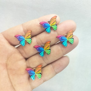 May include: Five rainbow butterfly charms with a silver metal finish. The butterflies have a detailed design with black outlines and a rainbow colour scheme.
