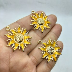 Könnte beinhalten: Drei goldfarbene Metall-Sonnenanhänger mit gelber Emaille. Jeder Anhänger zeigt eine stilisierte Sonne mit einem Gesicht in der Mitte.