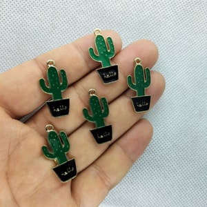 Puede incluir: Cinco abalorios de cactus de tono dorado con macetas negras y detalles de cactus verdes. Cada abalorio tiene la palabra "hello" escrita en la maceta.