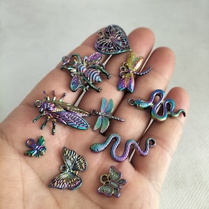 May include: Assortment of iridescent metal charms featuring a variety of nature-inspired designs, including butterflies, dragonflies, a bee, a cicada, and snakes. The charms are all in a rainbow iridescent finish.