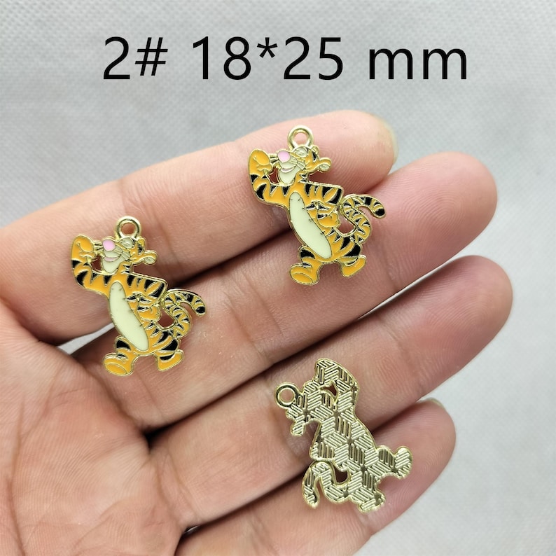 May include: Three Tigger-shaped charms. Two are yellow with black stripes and white bellies, and one is gold-colored with a textured pattern. The charms are approximately 0.7 x 1 inch in size. The text "2# 18*25 mm" is at the top.