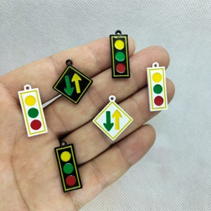 Pu&ograve; includere: Cinque ciondoli diversi a forma di semaforo e segnale stradale. I ciondoli sono in metallo e hanno uno schema di colori bianco, nero e verde. I ciondoli hanno la forma di semafori e segnali stradali.