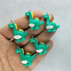 Può includere: Cinque ciondoli di dinosauro verdi con accenti gialli e pancia bianca. Ogni ciondolo ha un anello d'argento per attaccarlo a una collana, un braccialetto o altri gioielli.