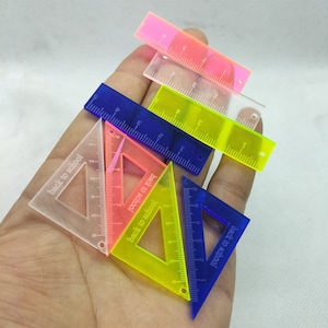 May include: A set of six colorful plastic rulers and protractors with the words "back to school" printed on them. The rulers are in various colors, including pink, yellow, blue, and clear.