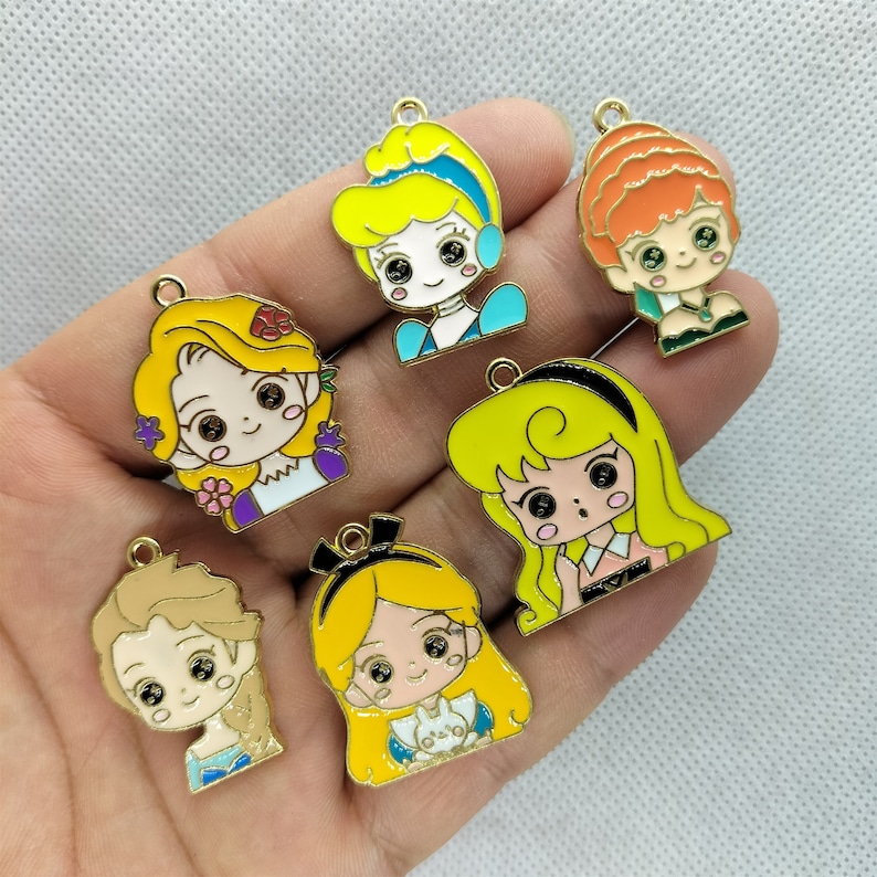 K&ouml;nnte beinhalten: Sieben goldfarbene Metall-Anh&auml;nger mit Comicfiguren mit gelbem Haar, blauen Augen und rosafarbenen Wangen. Die Figuren tragen verschiedene Outfits, darunter ein blaues Kleid, ein lila Kleid, ein gr&uuml;nes Kleid, ein wei&szlig;es Kleid und ein rosa Kleid. Die Anh&auml;nger sind perfekt, um Schmuck, Bastelarbeiten und anderen Projekten einen Hauch von Verspieltheit zu verleihen.