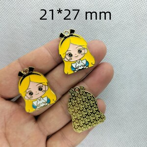 K&ouml;nnte beinhalten: Drei goldfarbene Metall-Anh&auml;nger mit einer Cartoon-Figur eines M&auml;dchens mit blonden Haaren und einem blauen Kleid. Die Anh&auml;nger sind 21 x 27 mm gro&szlig;.