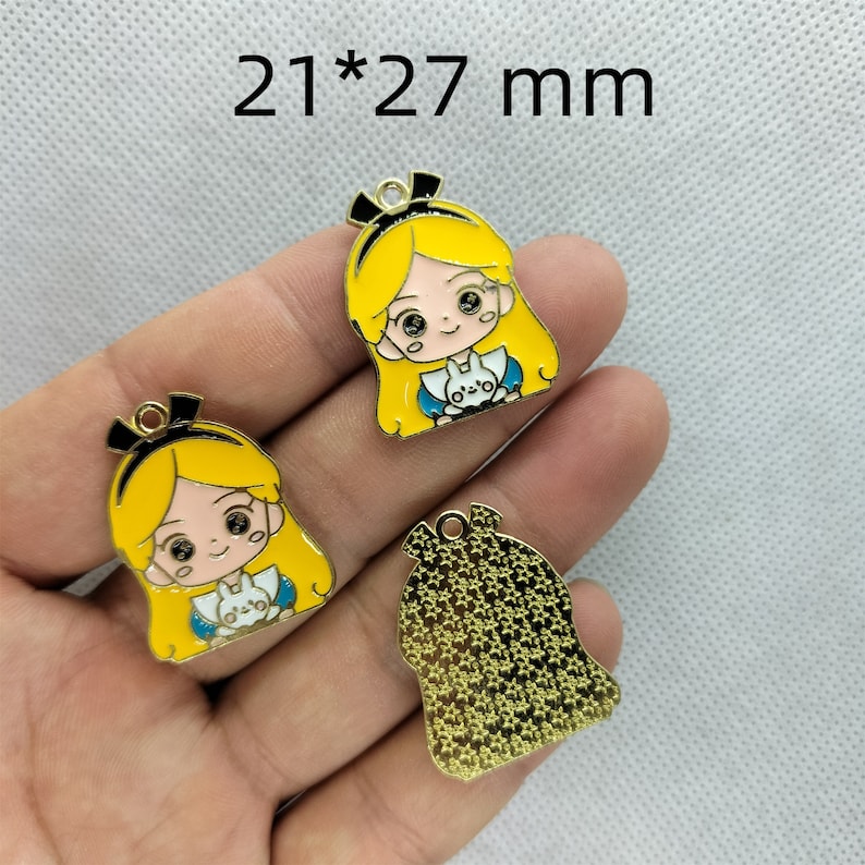 K&ouml;nnte beinhalten: Drei goldfarbene Metall-Anh&auml;nger mit einer Cartoon-Figur eines M&auml;dchens mit blonden Haaren und einem blauen Kleid. Die Anh&auml;nger sind 21 x 27 mm gro&szlig;.