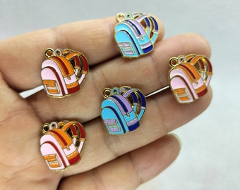 May include: Five gold-coloured backpack charms with enamel paint. The charms are in different colours: pink, orange, blue, light blue, and purple. Each charm has a gold loop for attaching to a chain or bracelet.