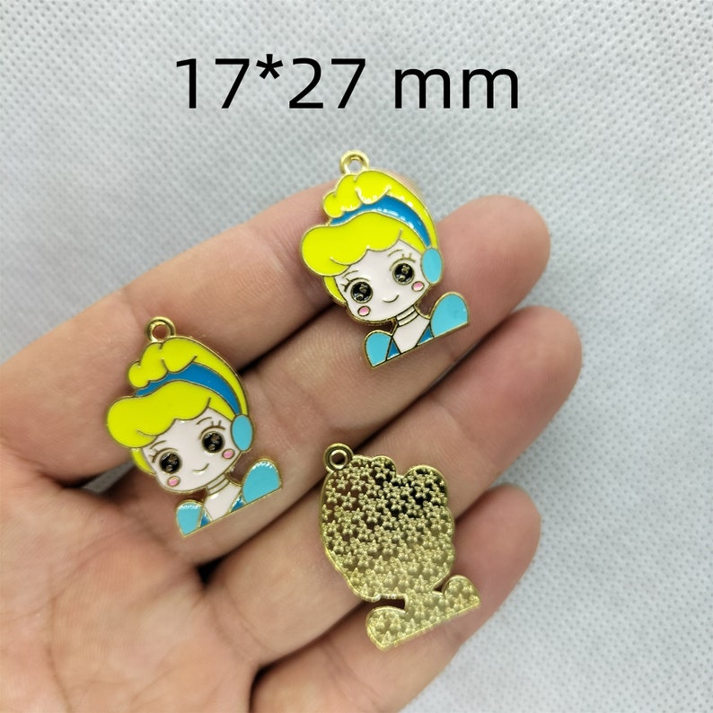 K&ouml;nnte beinhalten: Drei goldfarbene Metall-Anh&auml;nger mit einer Comic-Prinzessin mit blonden Haaren, blauen Augen und einem blauen Kleid. Die Anh&auml;nger sind 17 mm x 27 mm gro&szlig;.
