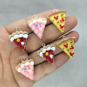 May include: A collection of miniature food charms, including pizza slices with red Mickey Mouse shapes and pie slices with pink and red fillings. Each charm has a silver loop for attaching to jewelry or other crafts.