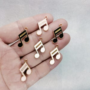 May include: Six gold-tone metal music note charms with black and white enamel. The charms are in the shape of a treble clef.