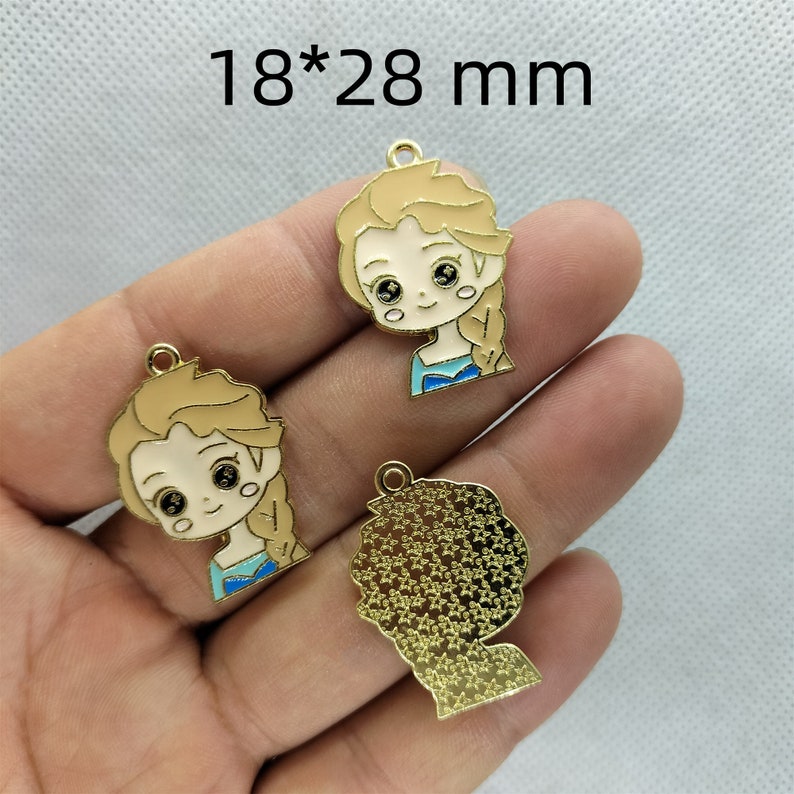 K&ouml;nnte beinhalten: Drei goldfarbene Metall-Anh&auml;nger, jeweils 18 x 28 mm gro&szlig;. Zwei Anh&auml;nger zeigen ein Cartoon-Bild eines M&auml;dchens mit blonden Haaren und blauen Augen, das ein blaues Kleid tr&auml;gt. Der dritte Anh&auml;nger ist eine Silhouette eines Personenkopfes mit einer strukturierten Oberfl&auml;che.