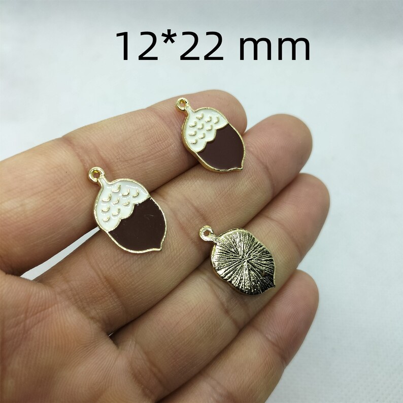 May include: Two gold-tone acorn charms with white and brown enamel. The charms are 12 mm by 22 mm.