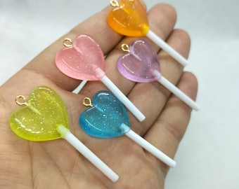 Può includere: Cinque lecca-lecca a forma di cuore con glitter, ognuno in un colore diverso: arancione, rosa, viola, giallo e blu. I lecca-lecca hanno cime dorate e bastoncini bianchi.