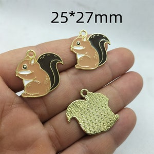May include: Three gold-colored metal charms in the shape of squirrels. Two charms are brown with black tails and white eyes. One charm is solid gold with a textured surface. The charms are 25*27mm in size.