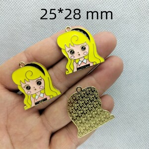 K&ouml;nnte beinhalten: Drei goldfarbene Metall-Anh&auml;nger, jeder misst 25 x 28 mm. Zwei Anh&auml;nger zeigen ein Cartoon-M&auml;dchen mit blonden Haaren, schwarzem Stirnband und einem rosa-wei&szlig;en Kleid. Der dritte Anh&auml;nger ist ein durchgehendes goldfarbenes Design.