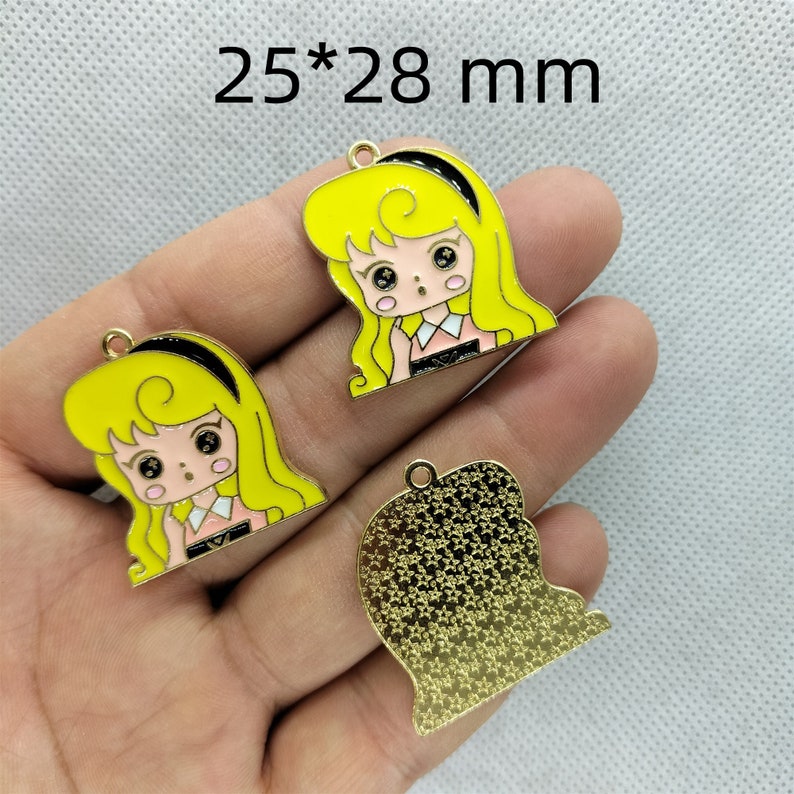 K&ouml;nnte beinhalten: Drei goldfarbene Metall-Anh&auml;nger, jeder misst 25 x 28 mm. Zwei Anh&auml;nger zeigen ein Cartoon-M&auml;dchen mit blonden Haaren, schwarzem Stirnband und einem rosa-wei&szlig;en Kleid. Der dritte Anh&auml;nger ist ein durchgehendes goldfarbenes Design.