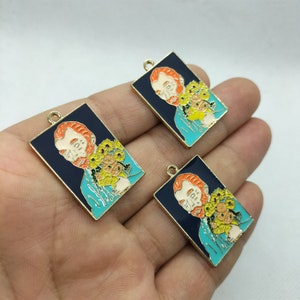 May include: Three gold-toned metal charms featuring a portrait of a man with a red beard and a bouquet of yellow flowers. The charms are rectangular and have a blue background with black outlines.