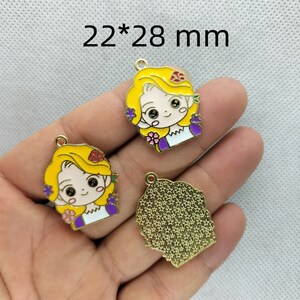 K&ouml;nnte beinhalten: Drei goldfarbene Metall-Anh&auml;nger mit einer Cartoon-M&auml;dchen mit langen blonden Haaren, die ein lila-wei&szlig;es Kleid tr&auml;gt. Die Anh&auml;nger sind 22 mm x 28 mm gro&szlig;.