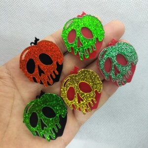 May include: Five glitter-covered red apple-shaped charms with a skull design. The apples are dripping with red paint and have different colored glitter: green, red, gold, and two shades of green.