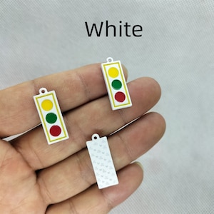 Pu&ograve; includere: Tre ciondoli in metallo bianco, due sono ciondoli di semaforo con luci rosse, gialle e verdi, e uno &egrave; un ciondolo con un motivo ripetitivo di piccoli cerchi.