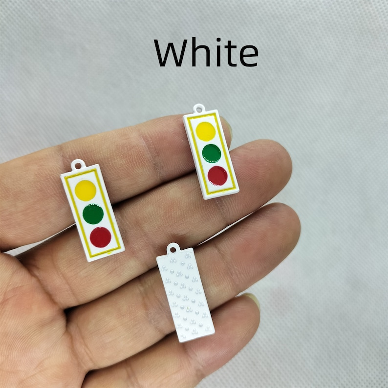 Pu&ograve; includere: Tre ciondoli in metallo bianco, due sono ciondoli di semaforo con luci rosse, gialle e verdi, e uno &egrave; un ciondolo con un motivo ripetitivo di piccoli cerchi.