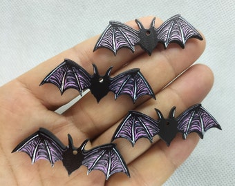 May include: Four black bat-shaped wooden ornaments with pink and white painted details. The bats have a hole at the top for hanging.