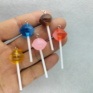 May include: Five colourful lollipop charms with silver tops and white sticks. The lollipops are in shades of blue, red, pink, brown, and yellow.