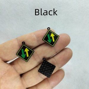 Pu&ograve; includere: Tre ciondoli in metallo nero con diversi design. Un ciondolo presenta un segnale stradale nero e giallo con due frecce che puntano in direzioni opposte. Un altro ciondolo presenta un segnale stradale nero e giallo con due frecce che puntano nella stessa direzione. Il terzo ciondolo &egrave; un quadrato nero pieno con un motivo di piccoli punti.