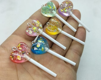 Pode incluir: Seis pirulitos de resina em forma de coração com detalhes de glitter em palitos brancos. Os pirulitos são de várias cores, incluindo rosa, azul, verde, amarelo e roxo.
