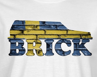 May include: White t-shirt with a blue and yellow brick pattern in the shape of a car and the word "BRICK" in blue letters.